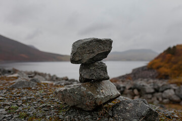 Balanced stone cairn by mountain lake with autumn hills in Welsh landscape