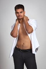 Attractive young brunette guy with short haircut in black trousers and white shirt posing in studio on white background