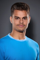 Fototapeta premium Portrait of an attractive young brunette with a short haircut and light stubble in a blue T-shirt on a gray background