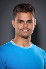 Fototapeta premium Portrait of an attractive young brunette with a short haircut and light stubble in a blue T-shirt on a gray background