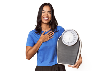 Filipino woman with scale in studio laughs out loudly keeping hand on chest.