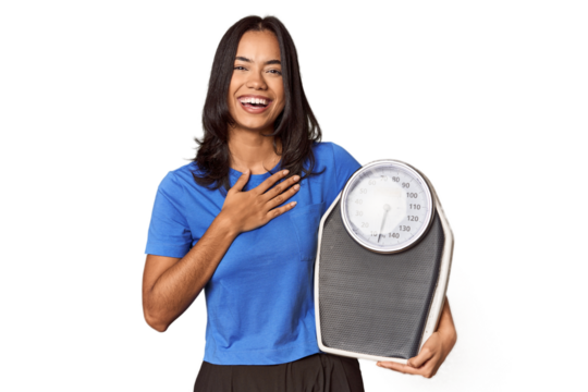 Filipino woman with scale in studio laughs out loudly keeping hand on chest.