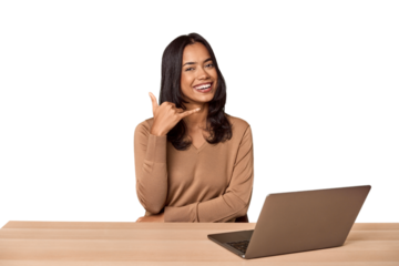 Filipino woman at desk with laptop showing a mobile phone call gesture with fingers.