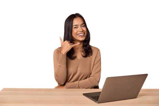 Filipino woman at desk with laptop showing a mobile phone call gesture with fingers.