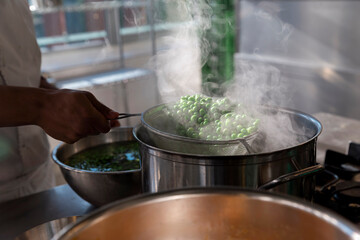 Fresh green peas steaming in metal strainer over cooking pot in professional kitchen
