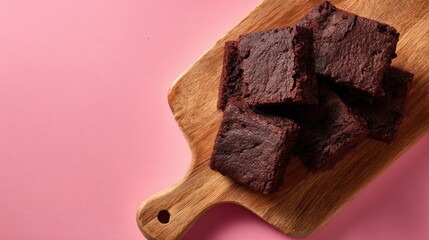 Brown squares of brownies on a light wooden cutting board against a pink background