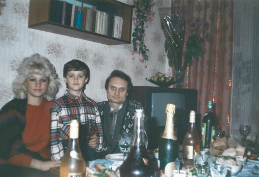 Young mother, father and son sitting at a festive table during Christmas celebration in early 1990s Ukraine, analog photography with warm film tones