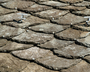 A close-up view of a traditional rooftop covered in overlapping, weathered slate shingles, creating a beautiful and intricate texture.