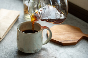 光と影の中でコーヒーをカップにそそぐ