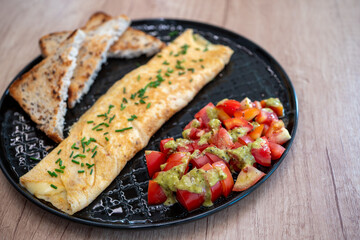 Healthy breakfast with folded omelette, fresh tomato salad with avocado dressing, and whole grain toast served on black plate, balanced meal rich in protein and fiber.