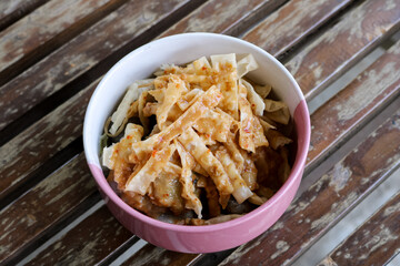 high angle photo from a close distance of a bowl of wonton skin or flour chips sprinkled with peanut sauce arranged on a wooden chair