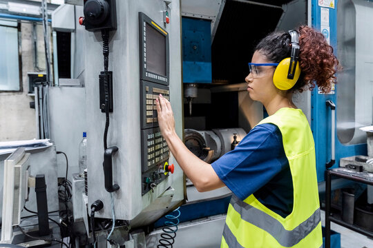 Maintenance engineer in protective workwear operating CNC machine in modern factory