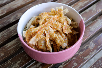 high angle photo from a close distance of a bowl of wonton skin or flour chips sprinkled with peanut sauce arranged on a wooden chair