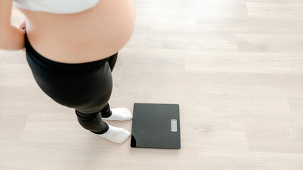 Pregnant woman monitoring weight on floor scale