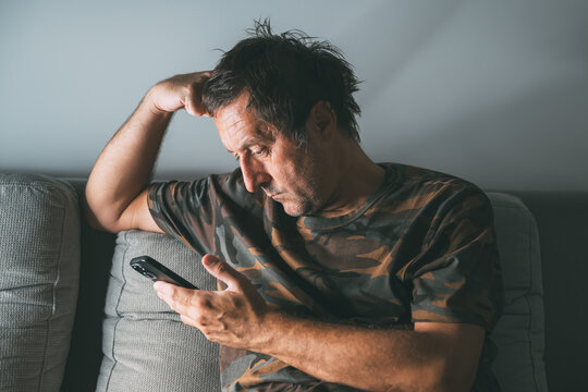 Middle-aged male using smartphone at home to explore social media content, low light - Powered by Adobe