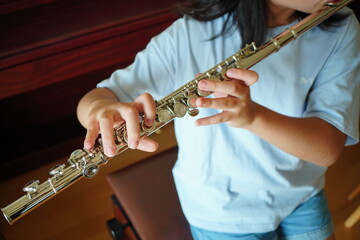 Close-up of a child playing the flute indoors, focus on hands and instrument, learning music and practicing performance