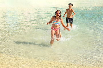 children joyfully playing in the water at the beach. With the sun shining and waves gently lapping at the shore, their laughter fills the air as they splash and play together