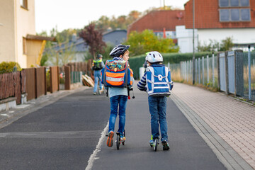 Two school kid boys in safety helmet riding with scooter in the city with backpack on sunny day....