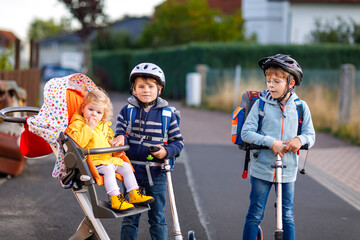 Two little school kid boys and cute toddler girl going to school. Tiny child sister sitting in pram. Brothers riding on scooter. Happy healthy amily of three children. © Irina Schmidt