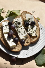 Close-up bread slices with cottage cheese and grapes on plate on parchment paper among grapes and leaves, top view