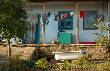 A charming rustic village house with laundry drying on the porch and an old bathtub in the yard, ideal for authentic rural storytelling.