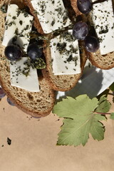 Close-up bread slices with cottage cheese and grapes on plate on parchment paper among grapes and leaves, top view