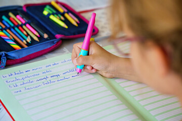 Little girl with eyeglasses focused on school homework, writing in a workbook at home. Real-life child learning, studying, and practicing writing skills.