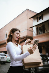A young elegant woman walks happily through a modern mall, holding shopping bags and phone, enjoying retail leisure, fashion, luxury, and style.