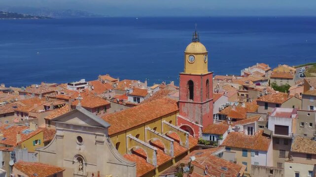 An aerial or elevated view captures the iconic glise Notre Dame de l'Assomption, a baroque style church with its distinctive red and yellow bell tower, nestled within the charming terracotta-roofed vi