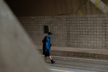 Woman wearing a blue scarf and black dress walking along a street.
