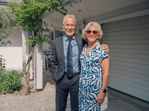 Married couple standing together and smiling outside their home in summer