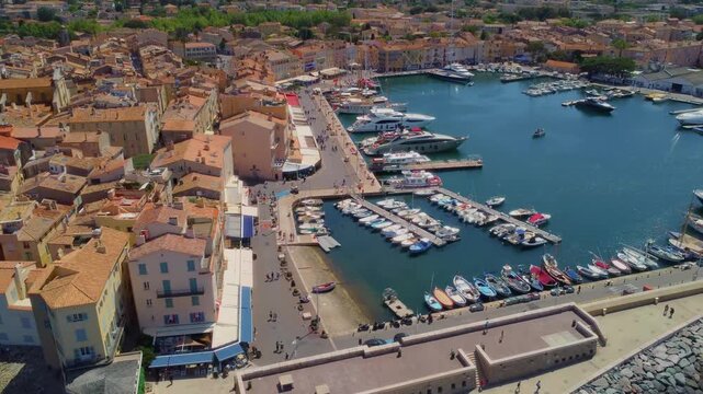 aerial view captures the vibrant Port de Saint Tropez, showcasing luxury yachts docked in the harbor alongside the picturesque, historic town with its charming terracotta rooftops.