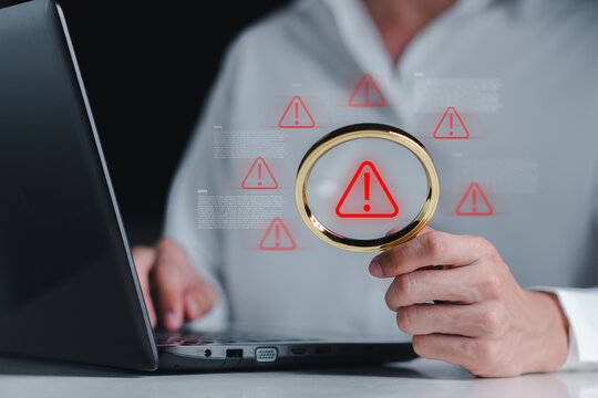 Cybersecurity analyst inspecting system warning alerts on a laptop using a magnifying glass. Concept of data breach detection, threat analysis, and digital security investigation process. - Powered by Adobe