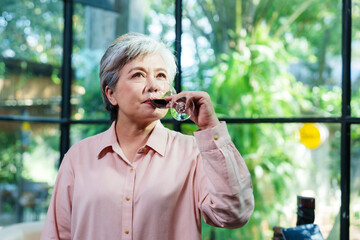 Senior Asian woman enjoying red wine cafe casual clothing indoor greenery peaceful relaxing cheerful lifestyle freedom retirement happiness nature tranquility environment drink enjoyment relaxation