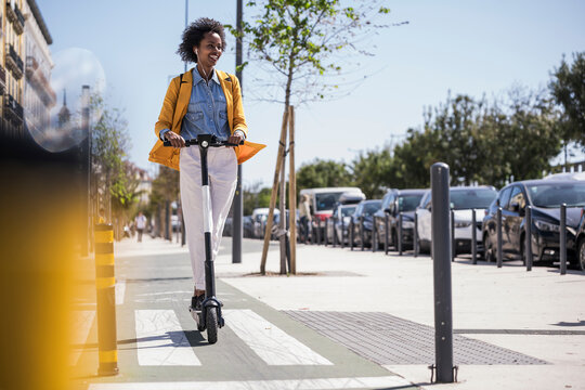 Smiling woman riding escooter in city on sunny day