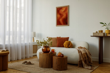 Cozy living room with cream sofa, orange pillows, plaid blanket and wooden tables with amber vases and decor.