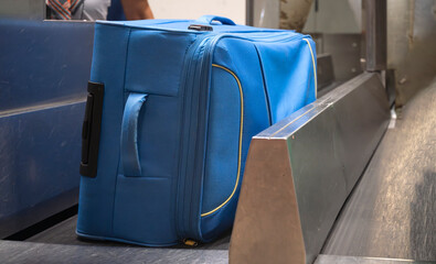 Blue suitcase on airport conveyor belt during luggage check-in process at departure terminal