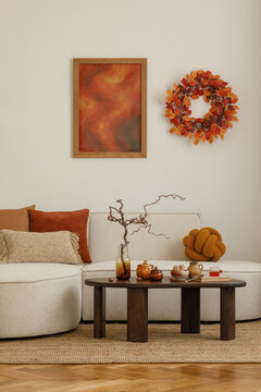 Autumn-inspired interior with beige sofa, orange cushions, mock up wall art and coffee table decorated with tea set and seasonal accents.