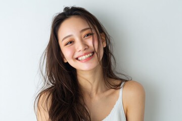 Naklejka premium Japanese woman with a radiant smile and clear skin, captured in a studio setting, reflects a youthful, effortless look with simple skincare and natural beauty.