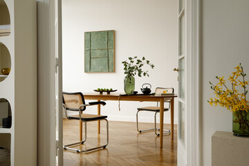 Dining room with wooden table, rattan chairs and green vase with eucalyptus, decorated with teapot and fruit in a bright modern interior.