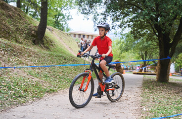 Determined boy in red shirt riding mountain bike on forest trail during outdoor cycling competition