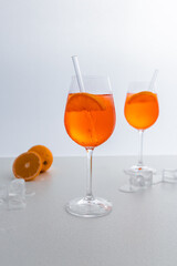Glas mit leuchtend orangefarbenem Aperol Spritz Cocktail, verziert mit Eiswürfeln, einer frischen Orangenscheibe und einem stilvollen Trinkhalm