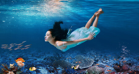 A woman gracefully swimming underwater in a flowing light blue dress.