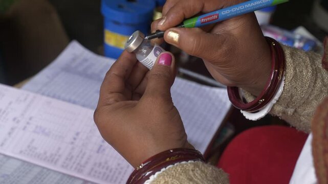 Social healthcare worker writing opening time on Tetanus vaccine vial at rural healthcare center, Lakhminia, Bihar