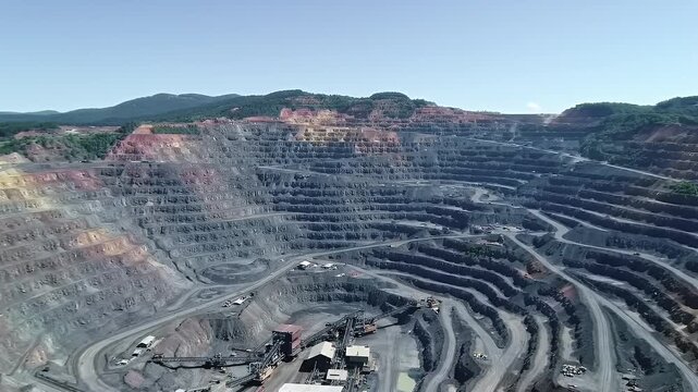 Expansive Open Pit Gold Mine Aerial View Featuring Terraced Earth and Winding Roads at Daytime Underneath Clear Blue Sky, Representing Resource Extraction and Environmental Transformation