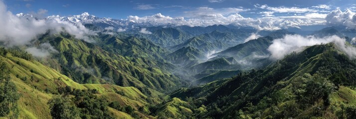 Panoramic view of lush green mountain ranges with valleys filled with mist, rolling hills, and distant snow-capped peaks under a partly cloudy sky