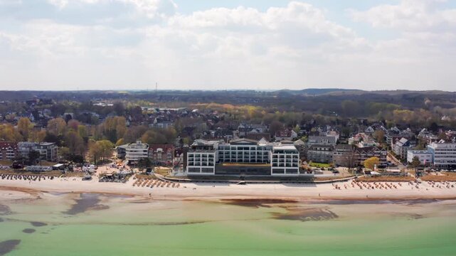 An aerial view of the modern Bayside Hotel situated directly on the sandy beach of Scharbeutz on the Baltic Sea coast. A popular German tourist destination with traditional 'Strandkorb' beach chairs.