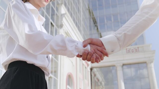 Business professionals engage in a handshake outside a modern building during a sunny day, symbolizing partnership and cooperation in urban setting