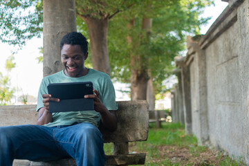 Obraz premium Casual African man playing mobile games on his smartphone, representing entertainment, technology, and modern digital lifestyle.