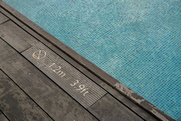 Close-up of poolside deck with depth marker 1.2 meters and blue mosaic tiles underwater, aquatic safety sign.